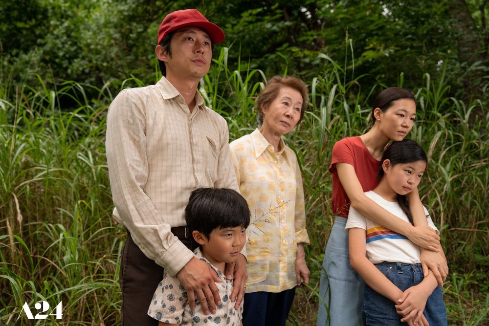 A family of five people stand in a wooded area.