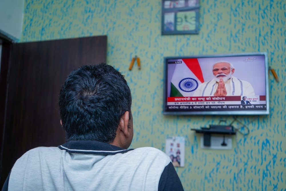 A man watches a television that is playing an announcement from PM Modi.