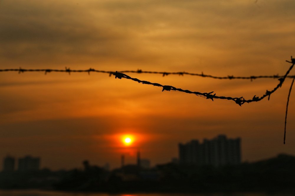 A piece of barbed wire in the foreground of a sunset over Mumbai