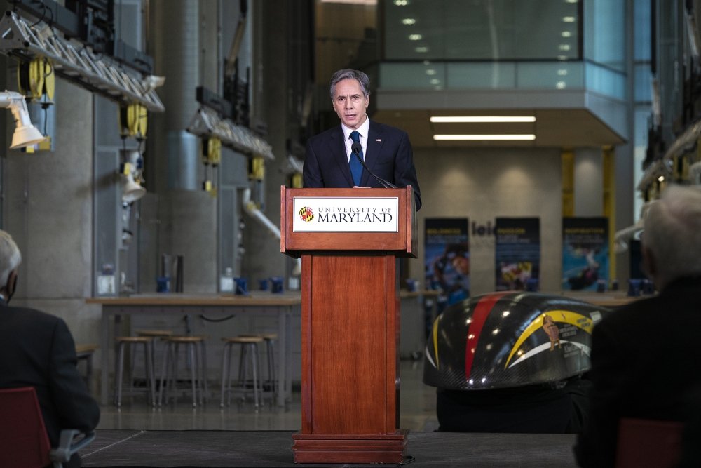 Secretary of State Antony Blinken stands at a podium with a University of Maryland logo on the front, delivering a speech.