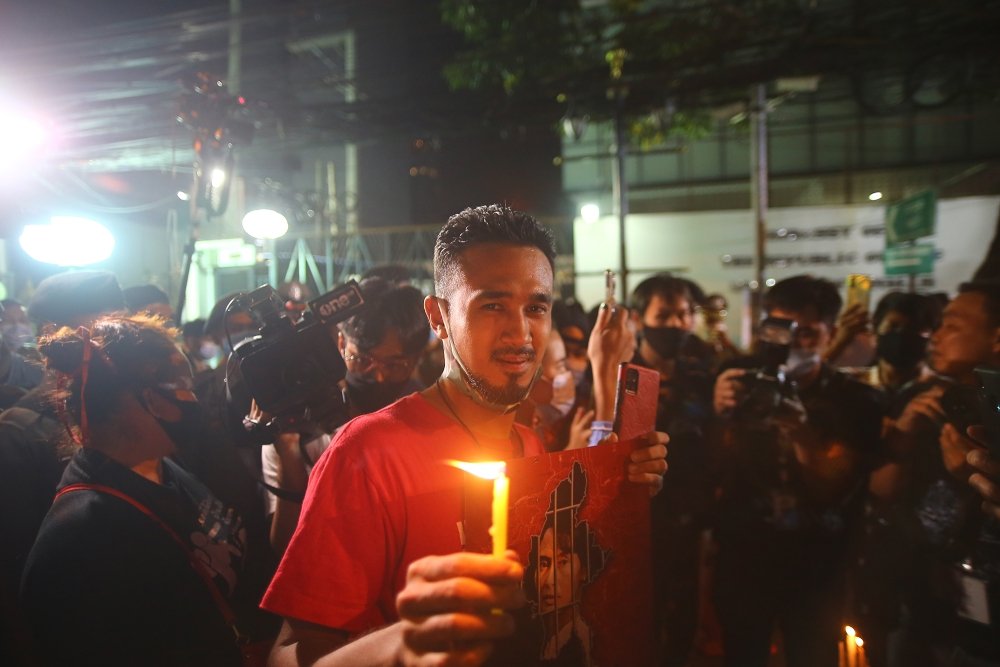 A man stands in a crowd of protestors holding a lit candle at night.