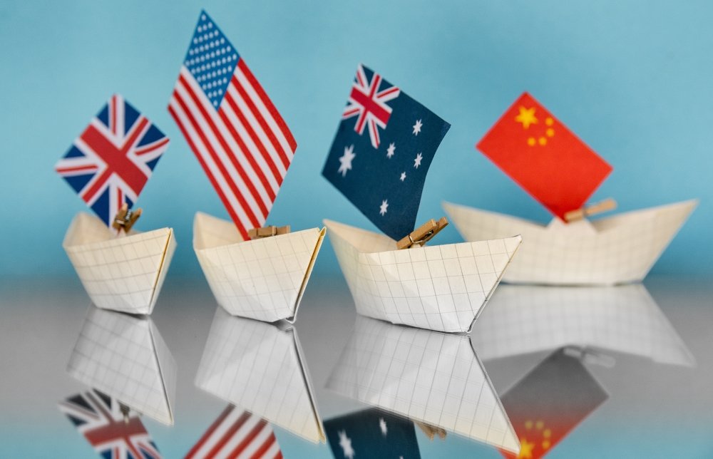 Four paper boats with national flags, from L to R, the UK, the US, Australia, and China.