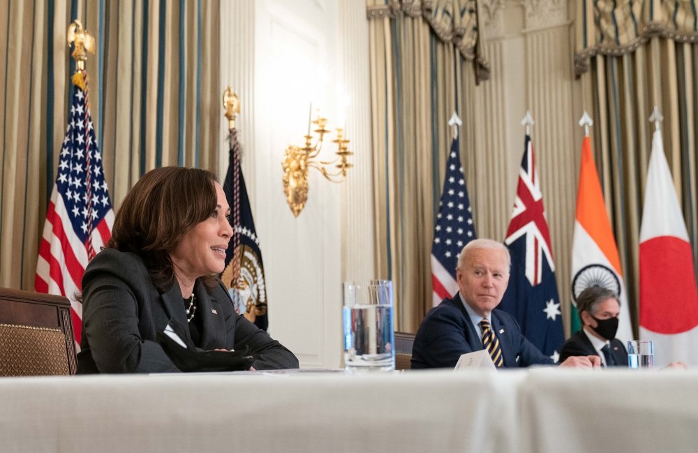 Harris, Biden, and Blinken sit at a table in front of the flags of the United States, Australia, India, and Japan.