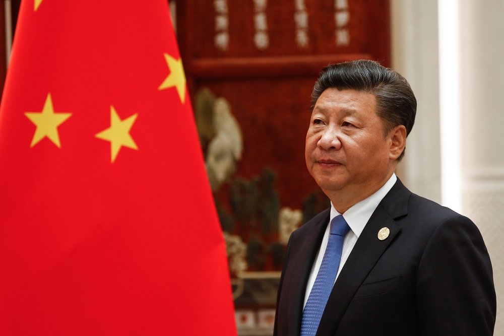 Xi Jinping standing next to the flag of China.