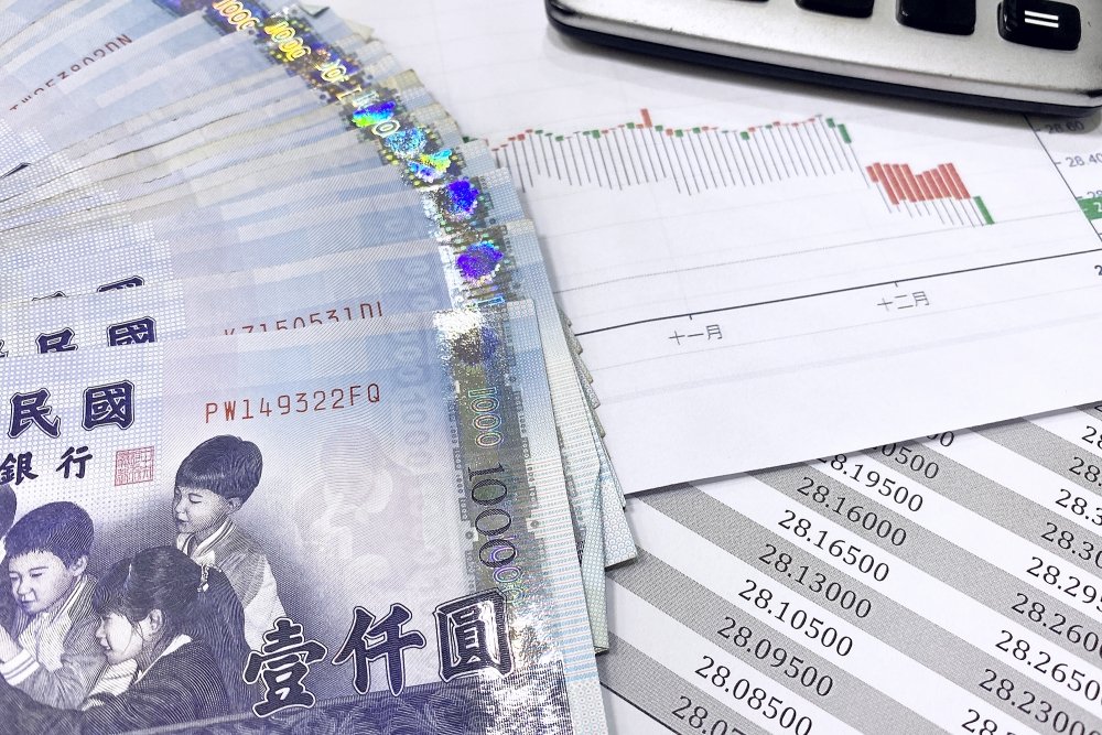 A stack of currency from Taiwan piled with spreadsheets and other reports.