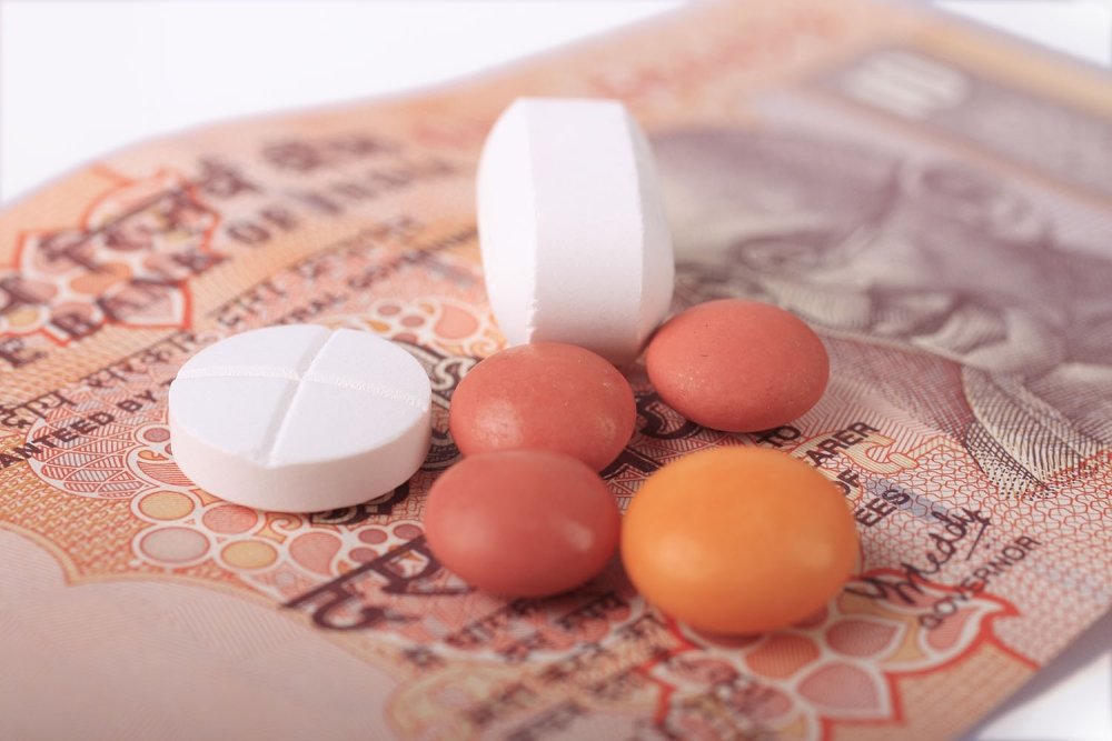 A group of different shaped pills sits on paper currency from India.