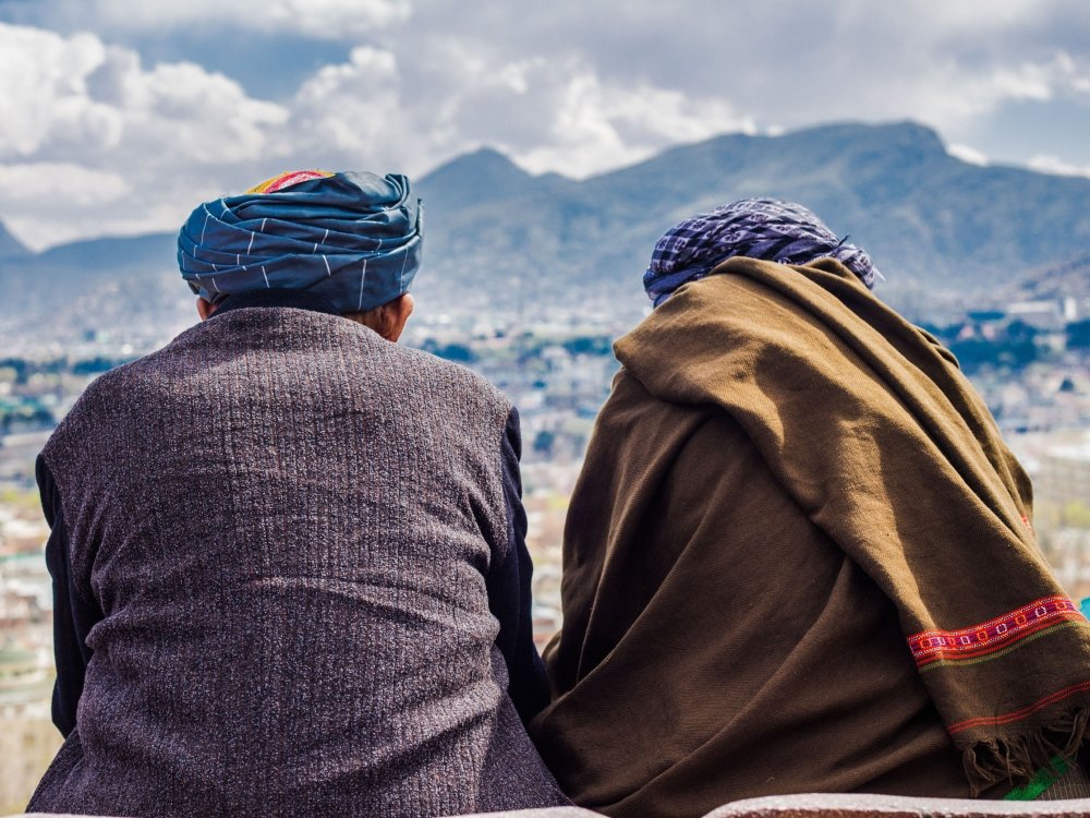 Two men sit with their backs to the camera, looking out at the Afghan mountains.