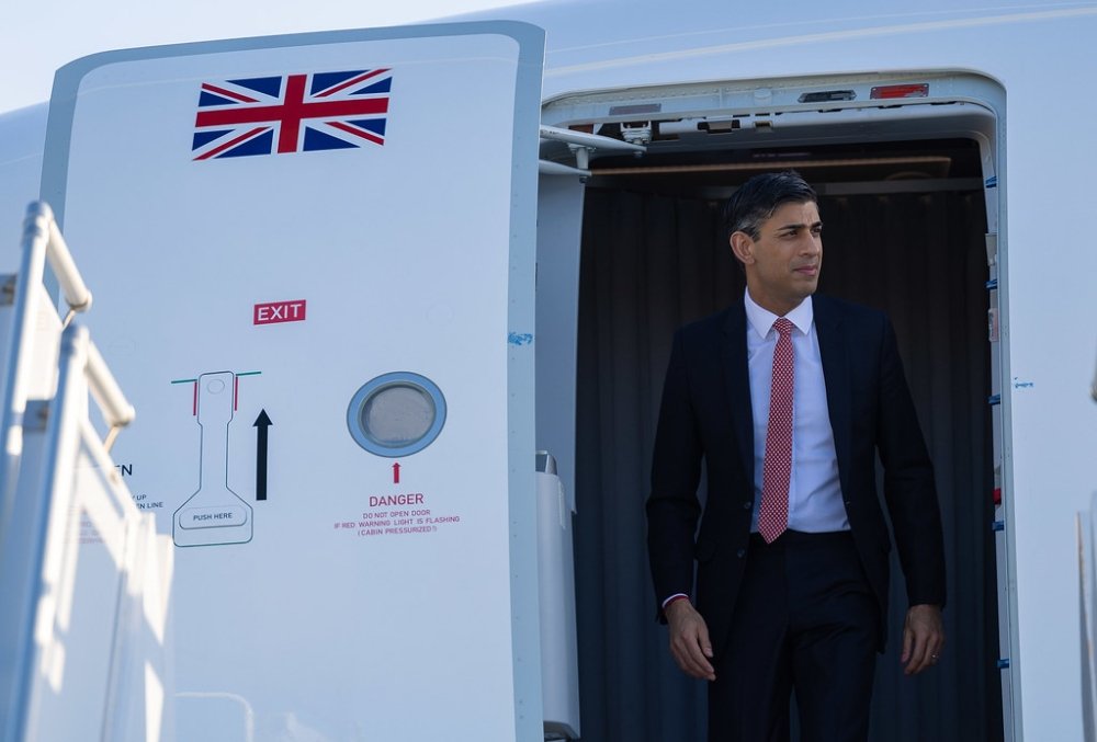 Prime Minister Rishi Sunak exits a plane with a UK flag visible on the door.