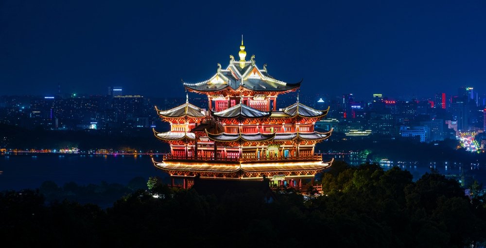 An ancient temple is lit up in front of a modern city skyline.