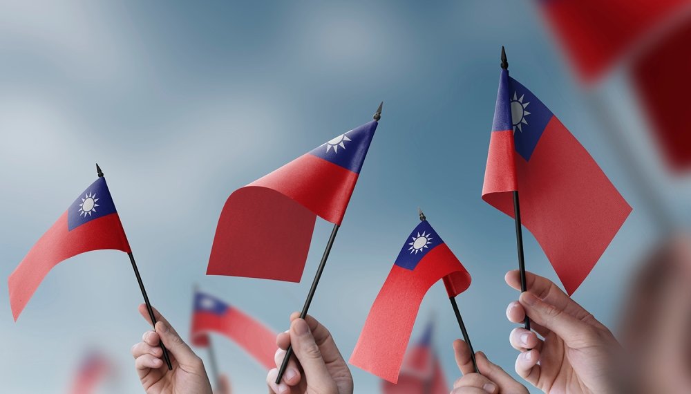 A close up of hands waving small Taiwanese flags.