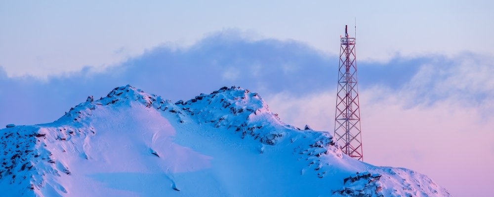 Telecommunication tower on the slope of a snowy mountain. Winter arctic landscape. View of the mountain top and the metal tower with antennas. Communication in the far north in the polar region.
