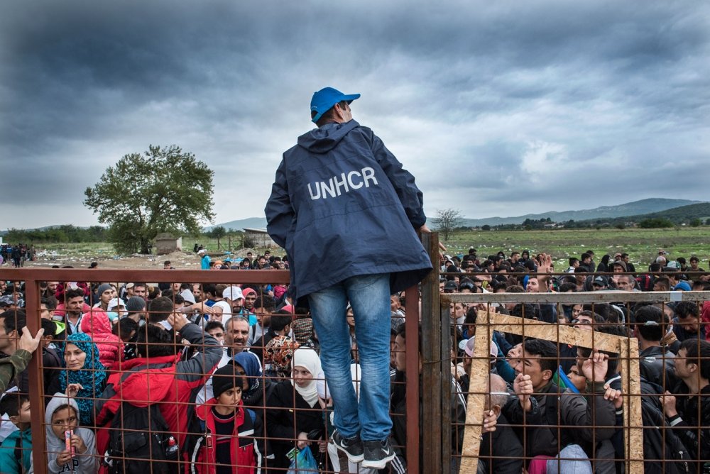 Gevjelija, Macedonia - September 26, 2015. A UNHCR employee talks to refugees as they wait during a rainstorm to enter inside a refugee camp near the town of Gevgelija at the Macedonian - Greek border