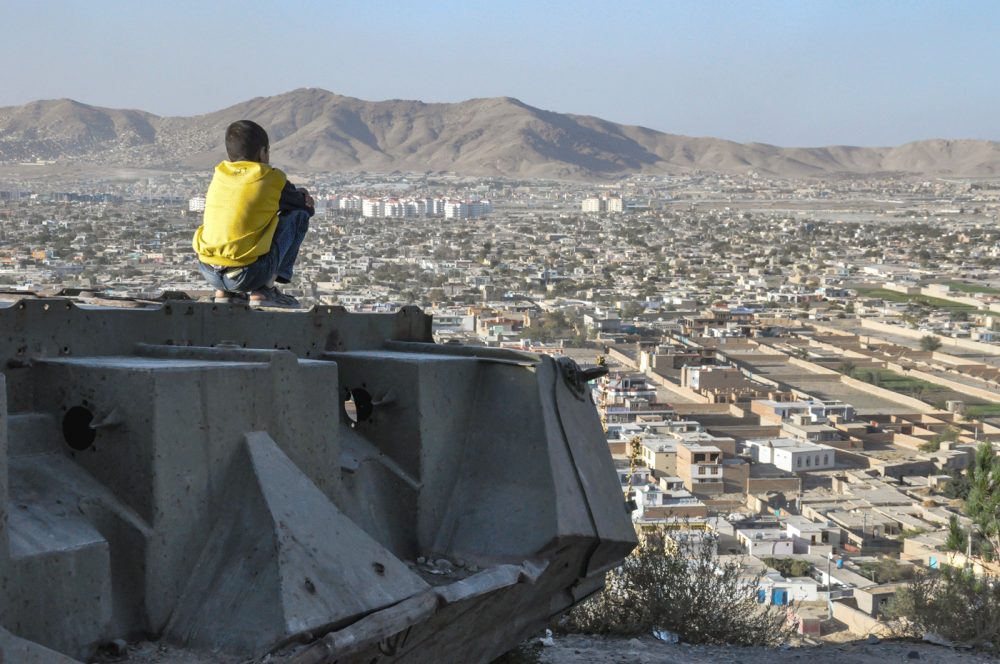 KABUL, AFGHANISTAN 2012: Boy sitting on Destroyed Tank on the hills over Kabul City in Afghanistan