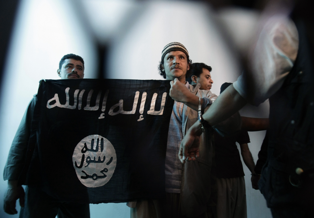 n this April 23, 2013 file photo, a suspected Yemeni al-Qaida militant, center, holds a banner as he stands behind bars during a court hearing in state security court in Sanaa, Yemen