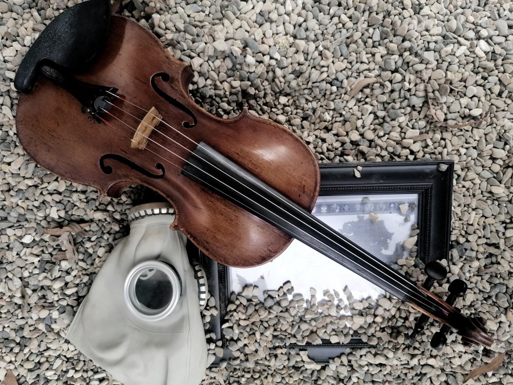 Image of a gas mask, violin and framed photo in gravel