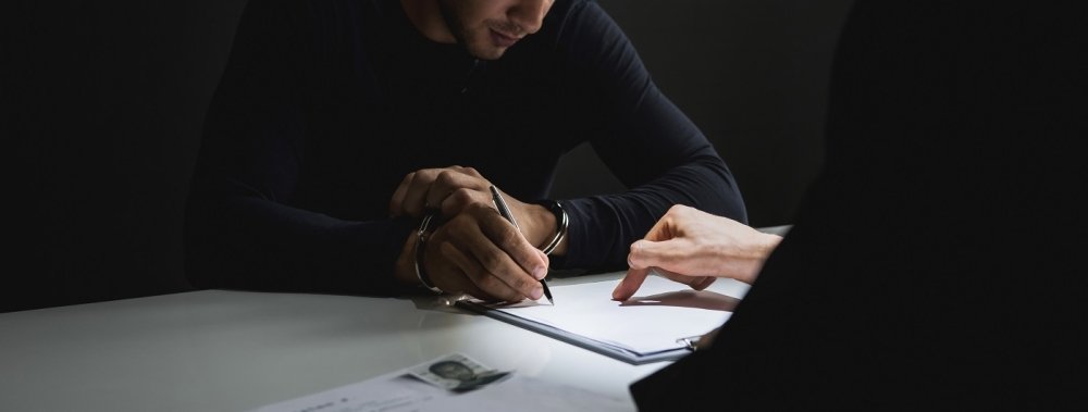  man with handcuffs signing a document in interrogation room