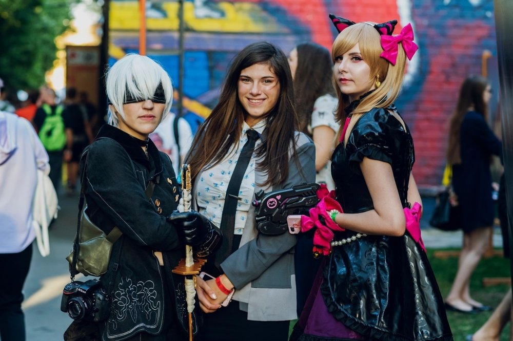 Three women dressed in fantasy and punk costumes standing in front of a mural at a festival in Kyiv