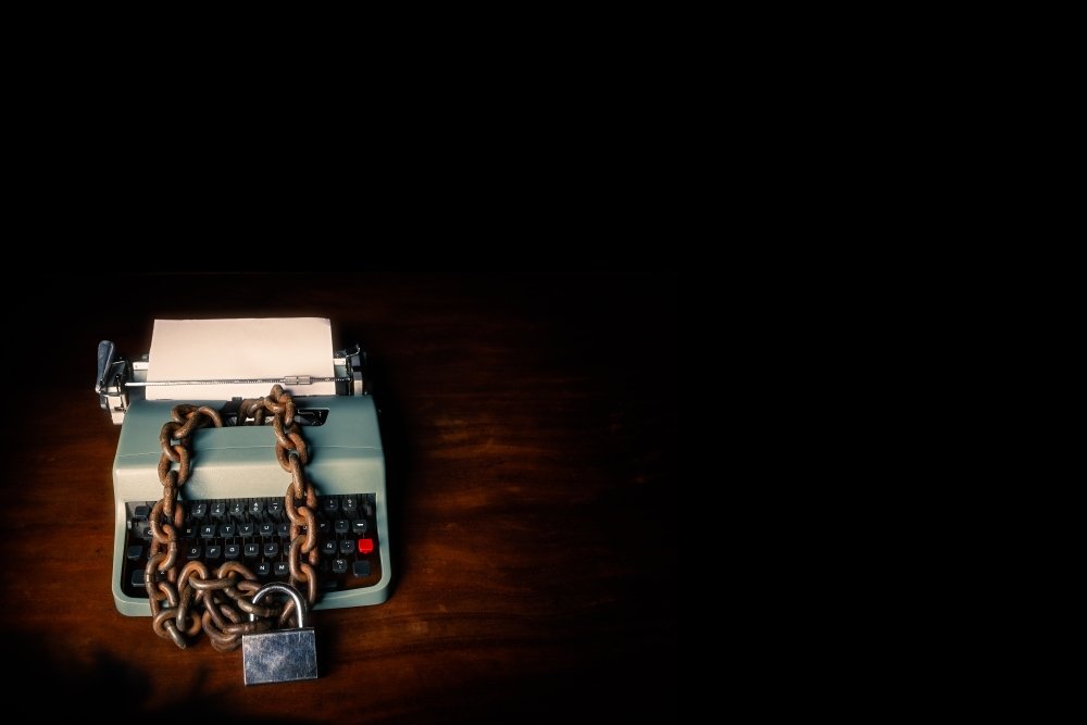 Typewriter locked with a chain and padlock on a black background