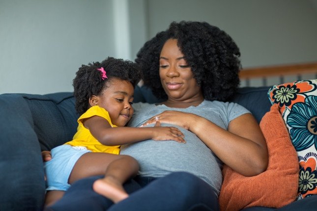 African American little girl holding her mother’s stomach.