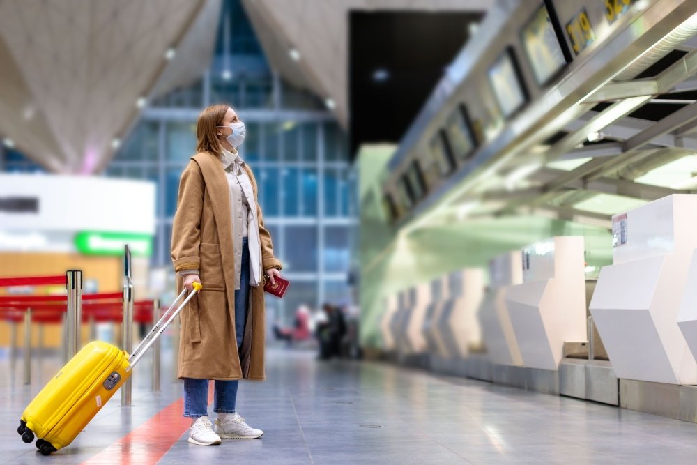 Woman with luggage stands at almost empty check-in counters at the airport terminal due to coronavirus pandemic/Covid-19 outbreak travel restrictions. Flight cancellation. Quarantine all over the world