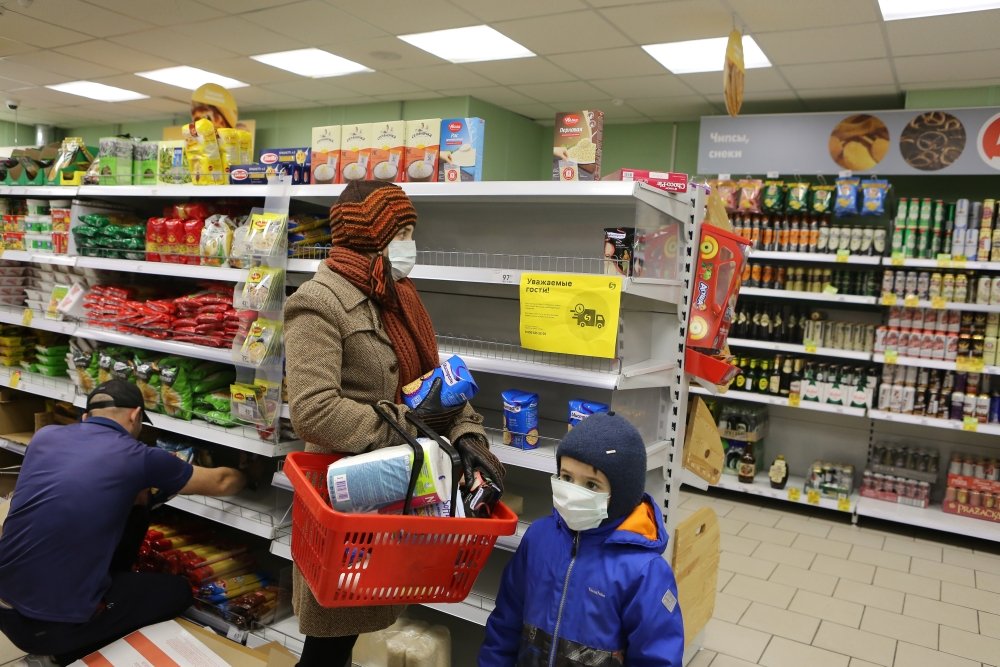 Shoppers in a Moscow grocery store where there are few products on shelves, holding buckwheat and toilet paper. 
