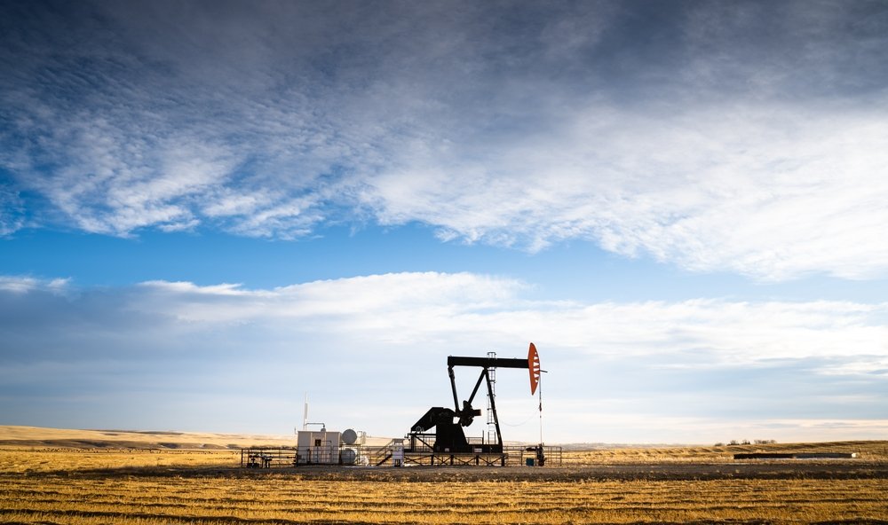 An industrial oil pump jack working on farm land under a morning sky