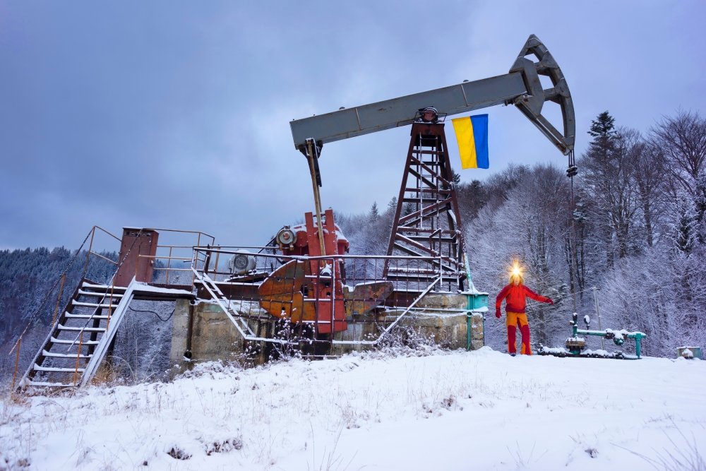 A working engineer at an oil and gas development of an old field checks the operation of mechanisms and control systems in the mountains after a winter in early spring. Flag of Ukraine yellow-blue.