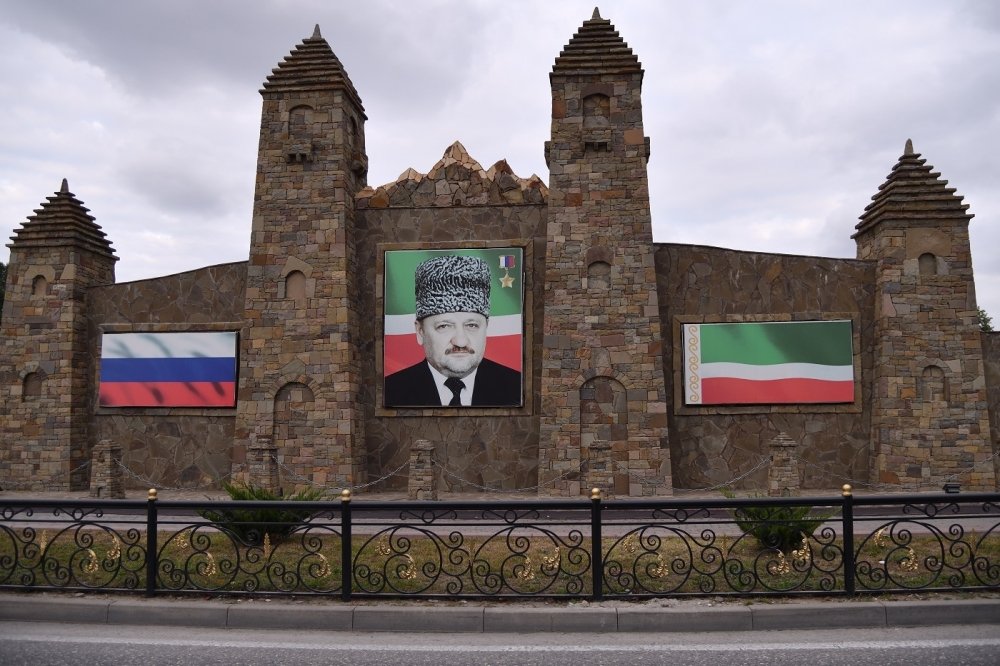Portrait of Akhmad Kadyrov on a old stone building next to Russian and Chechen Flags