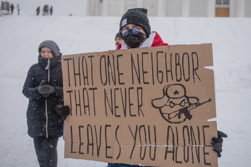 Protester in snow with sign that reads "That one neighbor that never leaves you alone" and a caricature representing the Russian state