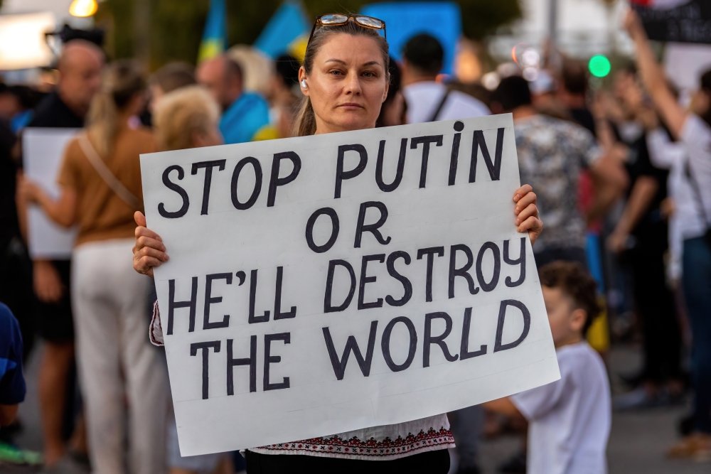 Woman holds a protest sign reading "stop Putin or he'll destroy the world"