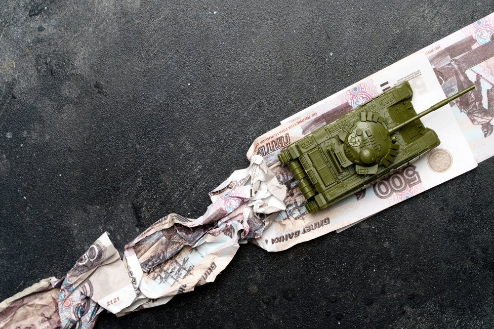 A toy tank runs over Russian ruble notes