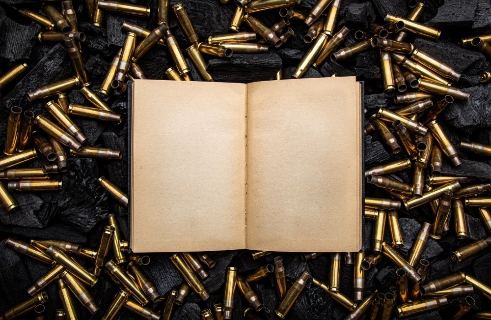 open book in a black hardcover with yellowed blank pages. Empty gun cases lying on charred coals.