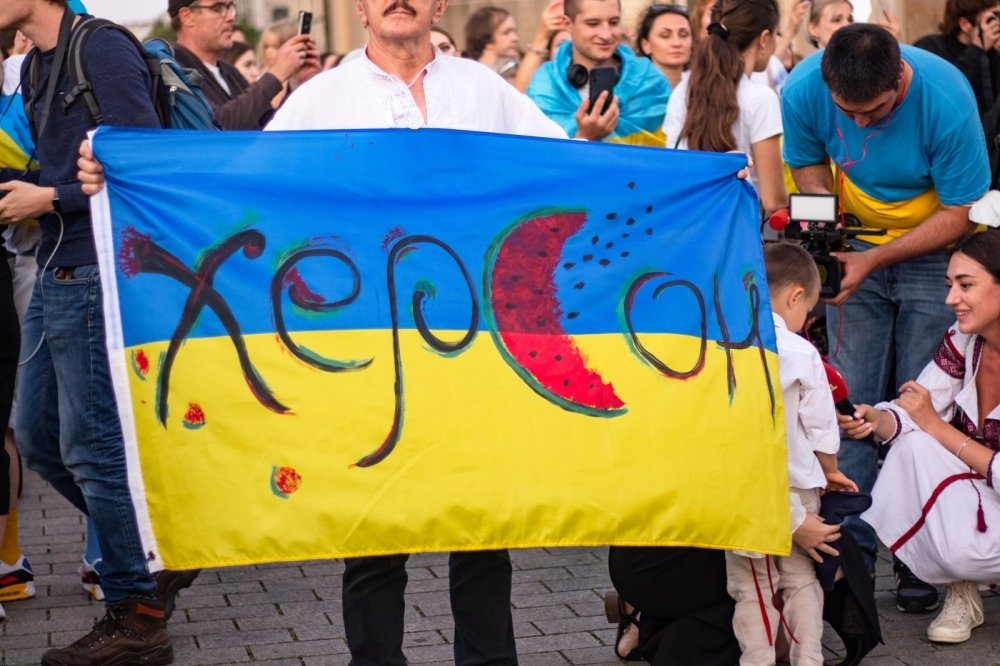 Person holding Ukrainian flag with text "Kherson" and watermelon motifs 