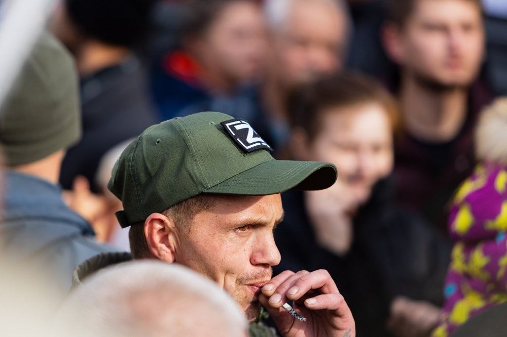 Man in crowd smoking a cigarette and wearing a hat in support of the special military operation