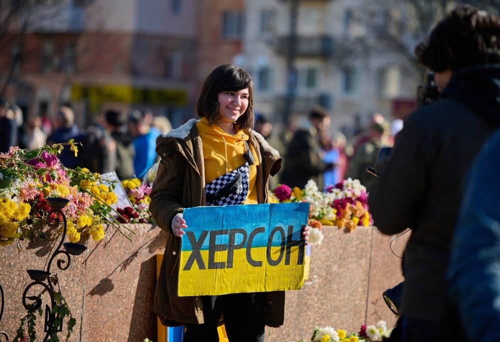 Woman holding sign with colors of Ukrainian flag and "Kherson" written in Cyrillic 
