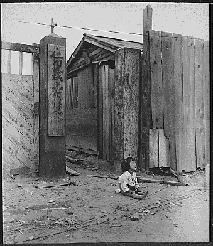 A black and white photo of a young girl sitting alone amid rubble, crying.