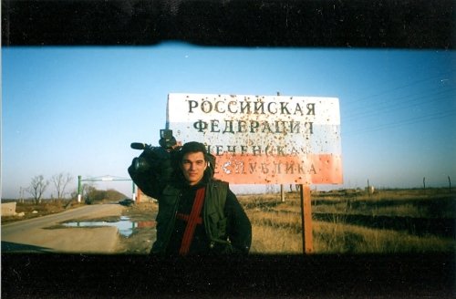 Man holding camera next to sign with Russian text