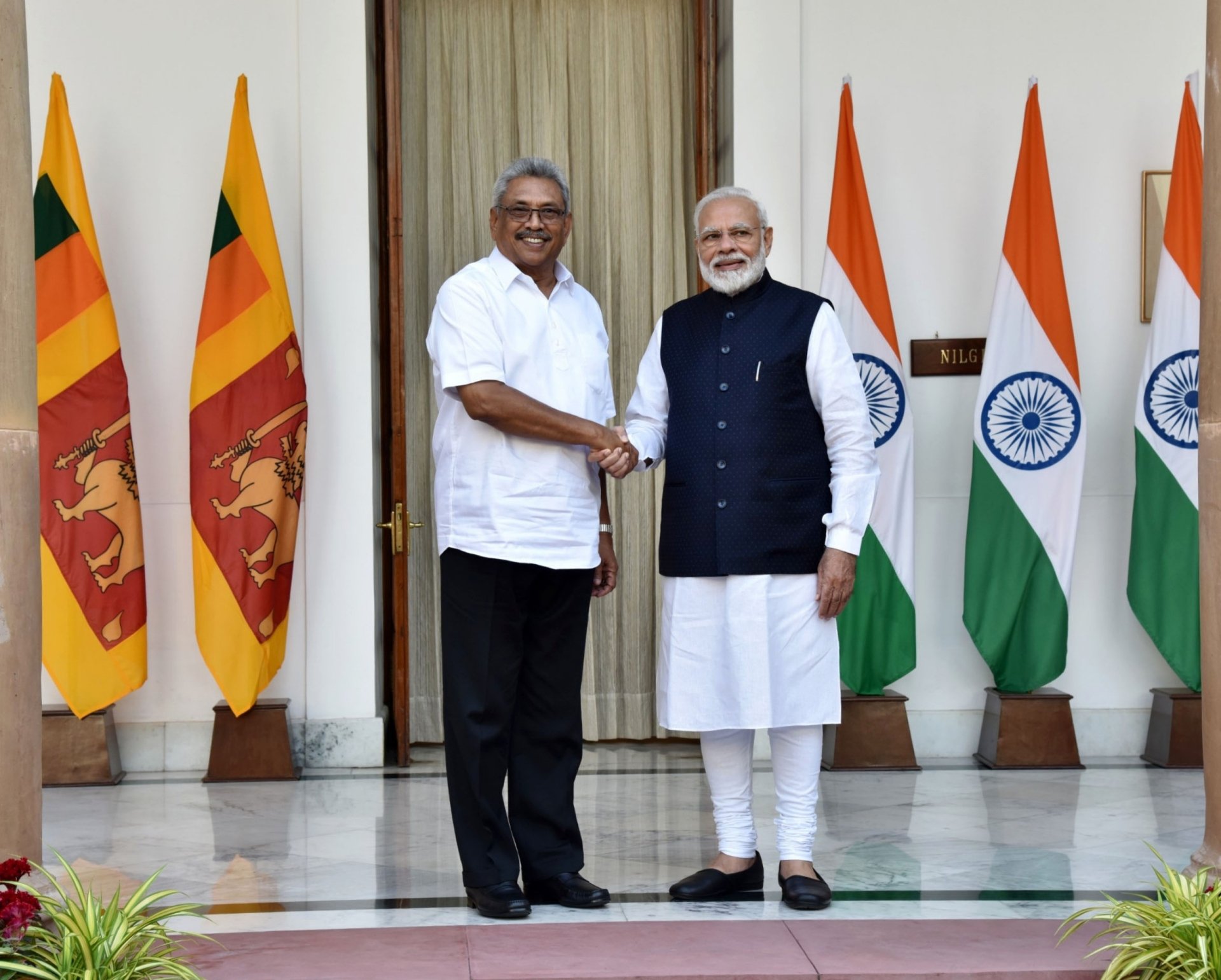 President Rajapaksa and PM Modi shaking hands in front of the flags of Sri Lanka and India