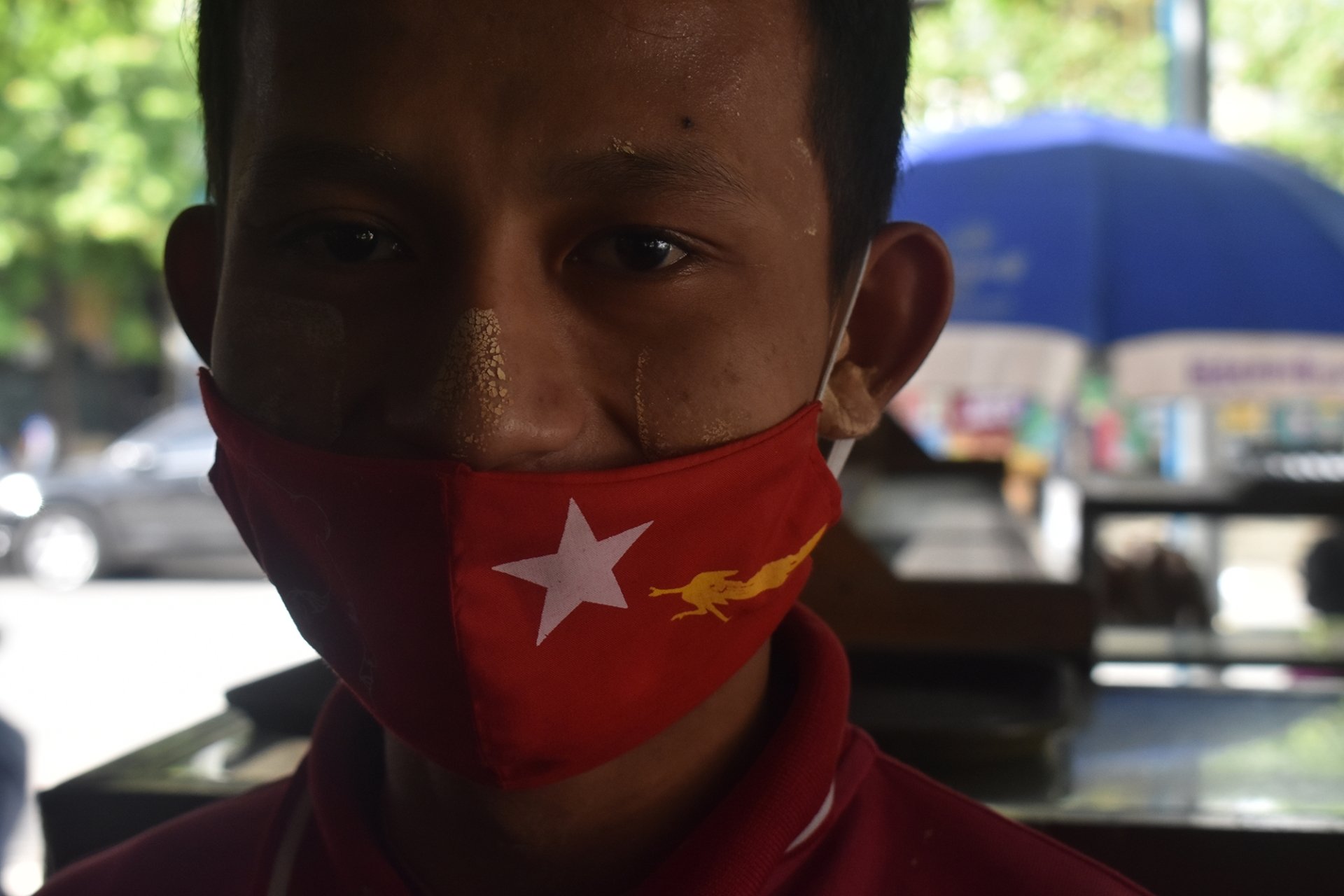 A man with a red face mask that has a white star and a gold peacock, the symbols of the NLD.