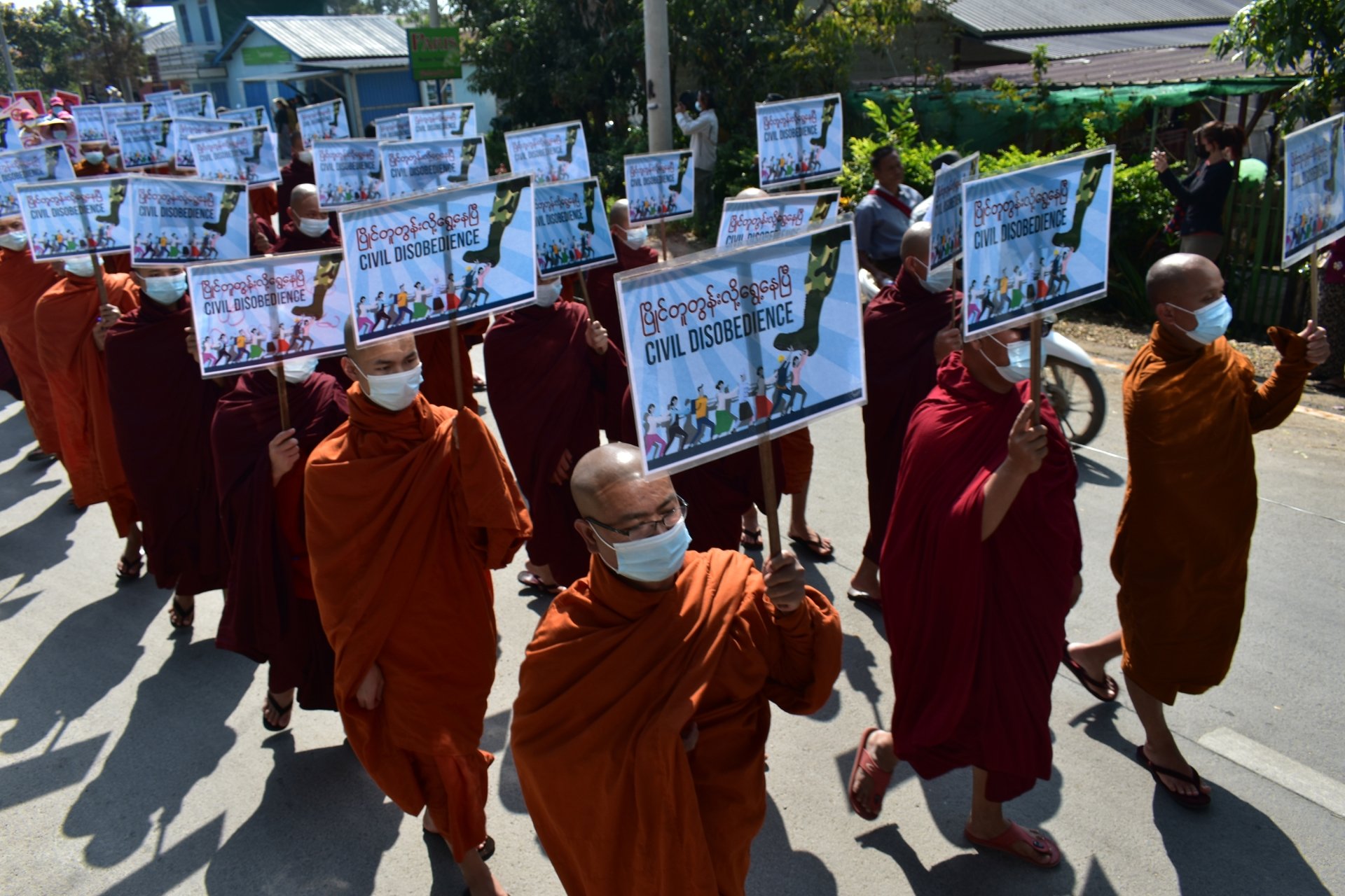 A grou pof monks in robes carrying protest signs as they march in the streets.