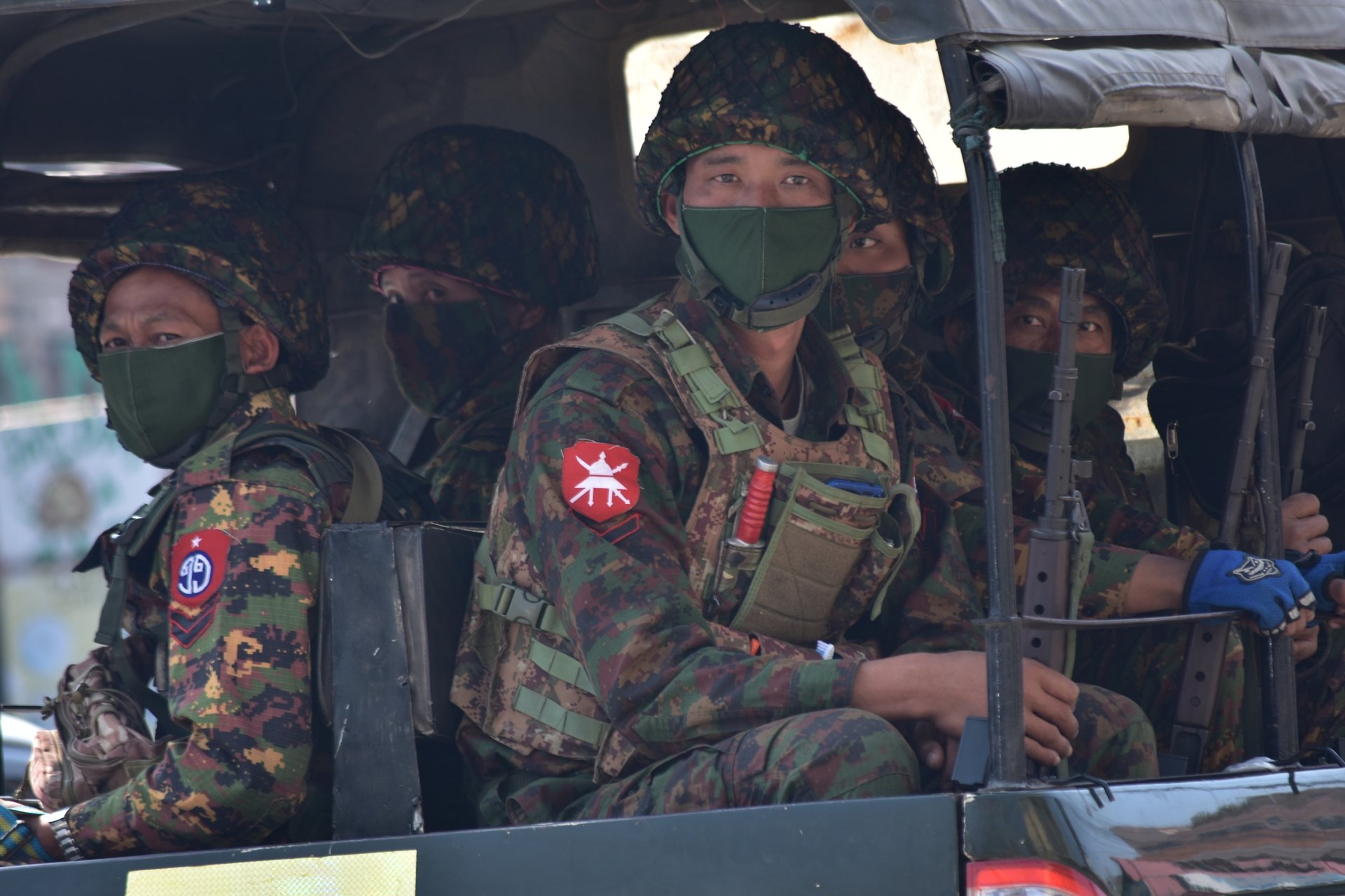 Soldiers in uniforms and masks sitting on a truck.