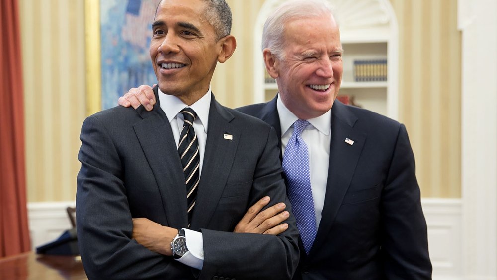 Joe Biden stands with his arm around President Obama in the Oval Office.
