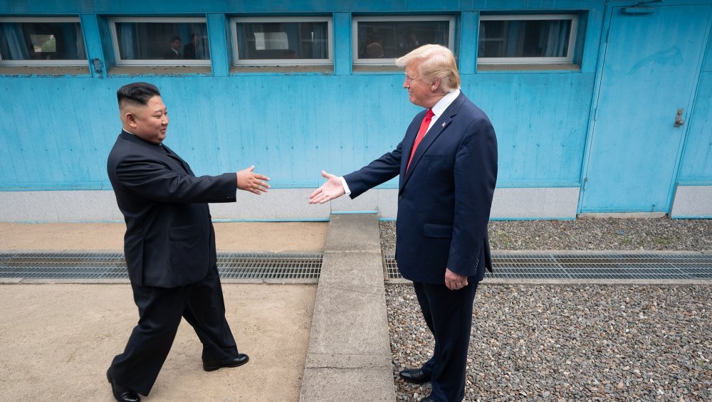 Chairman Kim Jong Un and President Donald Trump stand on either side of the DMZ border, reaching out to shake hands.