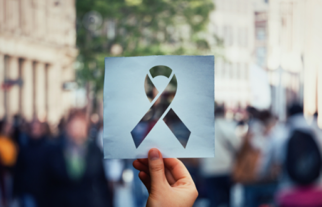 Image of hand holding a paper sheet with HIV red ribbon symbol over crowded street background