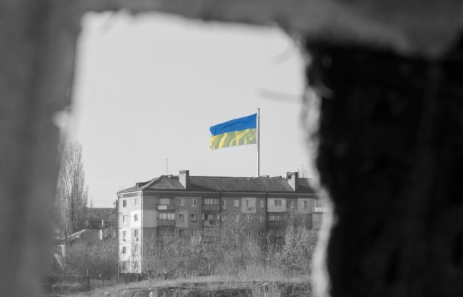 View through the window of the ruined house on the flag of Ukraine in the blue sky. Russia's aggression against Ukraine. The concept of peace after the war.f
