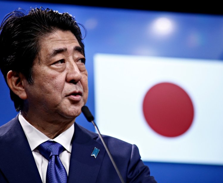 Prime Minister Shinzo Abe speaks in front of a Japanese flag at an event.