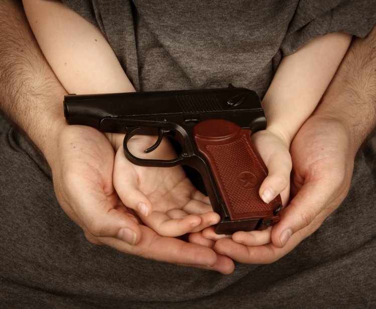 A man cradles a boy's hands while holding a gun.