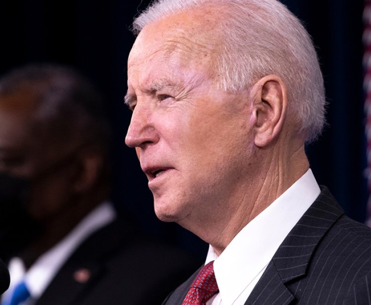 President Biden speaks at a lecturn in front of a background of American flags.