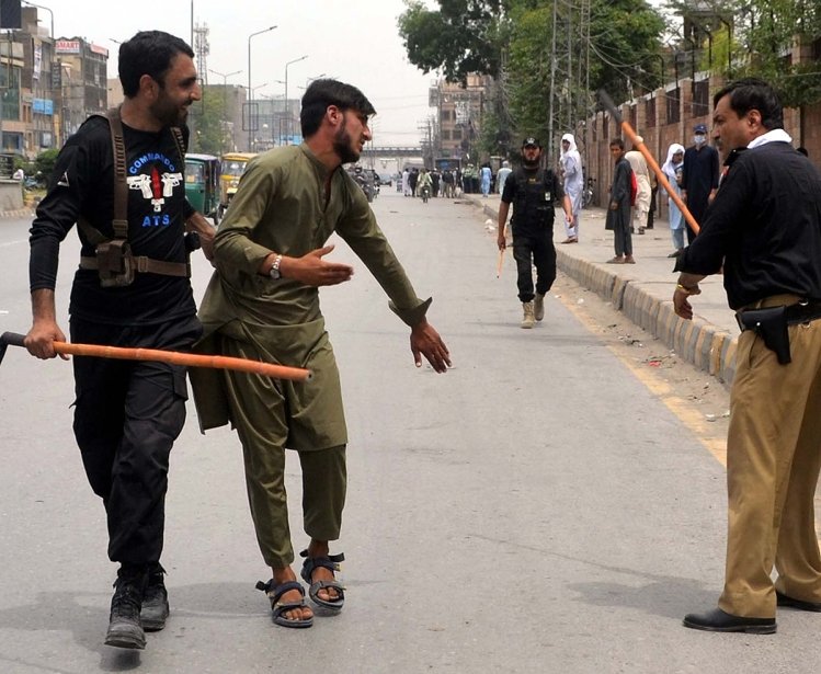 Two men with weapons are detaining another man on the street as people look on.