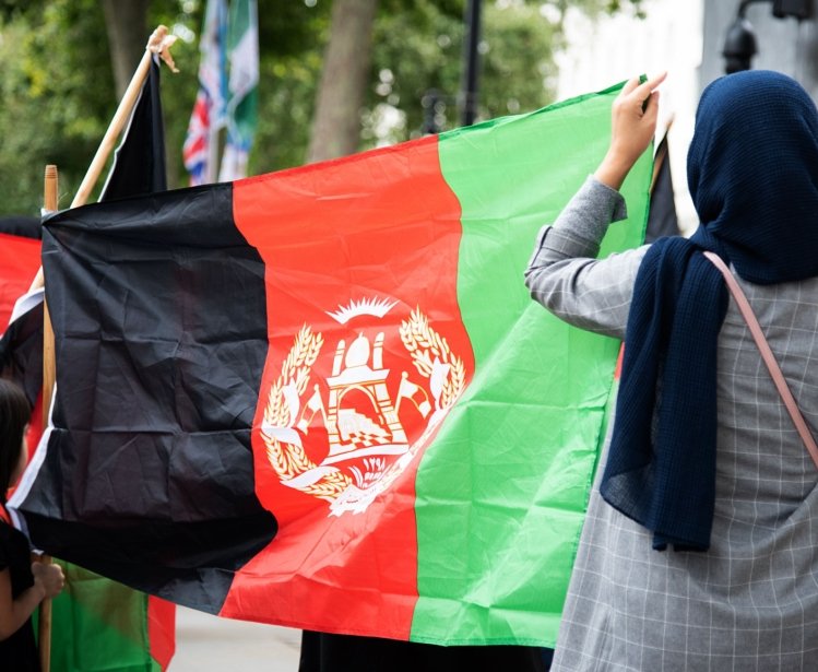 Two people with their backs to the camera are holding a large Afghan flag.